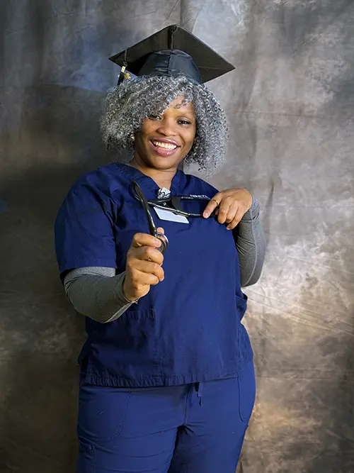 Herzing University healthcare graduate in scrubs holding a stethoscope and cap to celebrate graduation