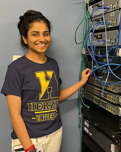 Herzing University technology student smiling while working with network servers and cables in a campus lab