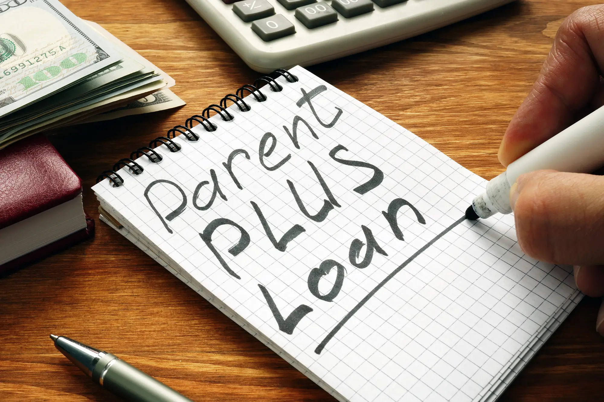  Parent PLUS loan written in notebook with cash and calculator, representing changes to federal student loan programs