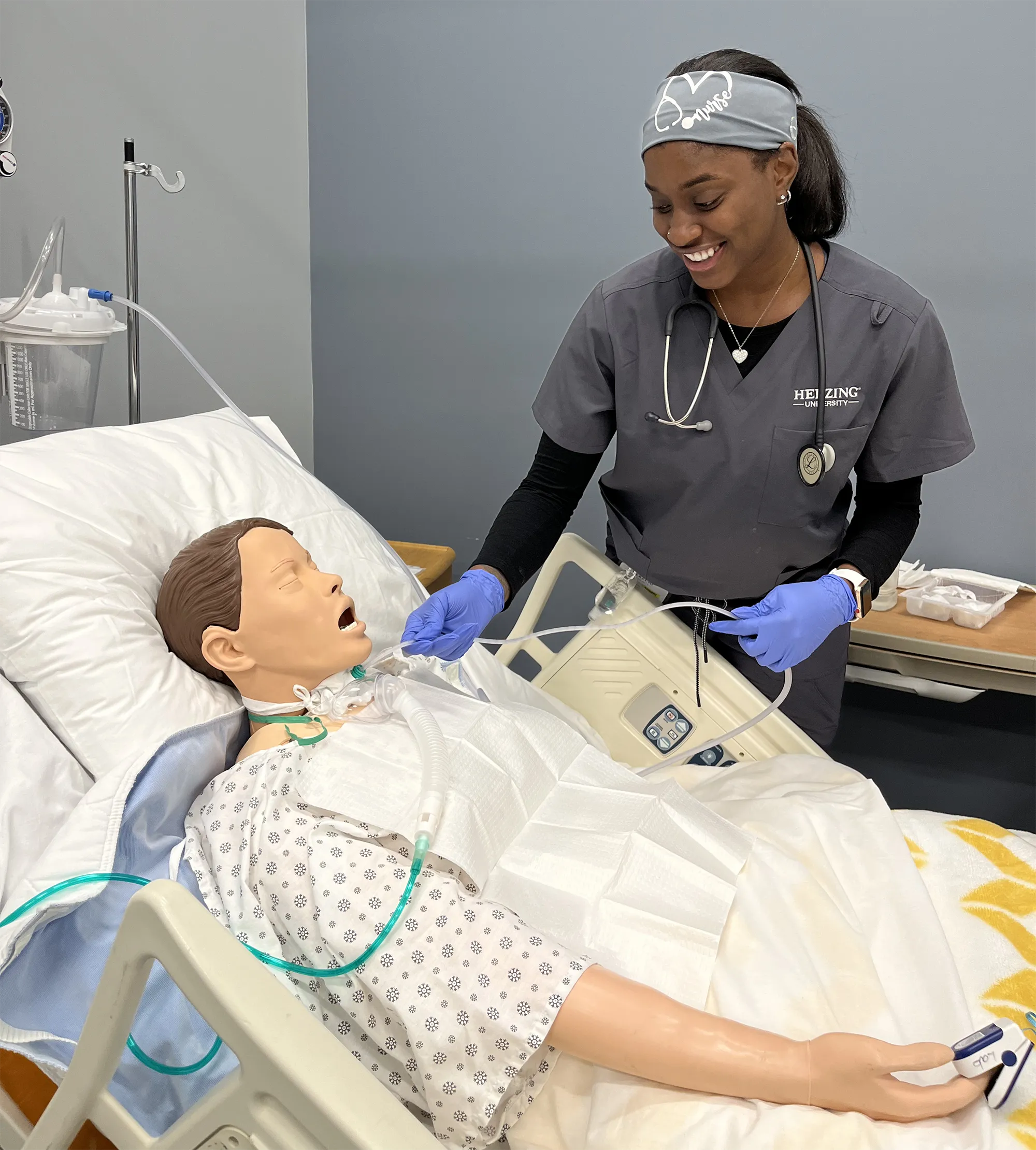 Herzing University nursing student provides hands-on care to a patient simulator during a clinical skills training exercise in a simulated hospital room.