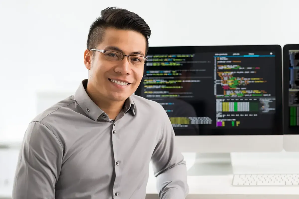 Computer programmer seated in front of two monitors showing coding software