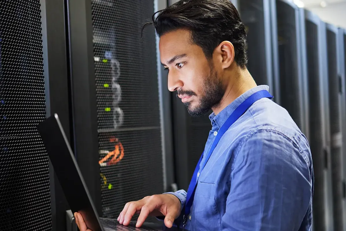 Cybersecurity manager reviewing server configuration while holding laptop