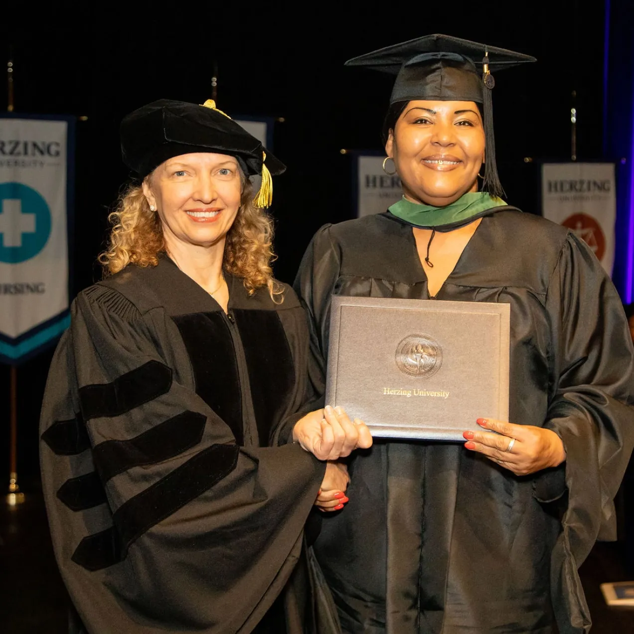 Herzing University President Renee Herzing shakes hands with a graduate in a cap and gown, celebrating his achievement during commencement.