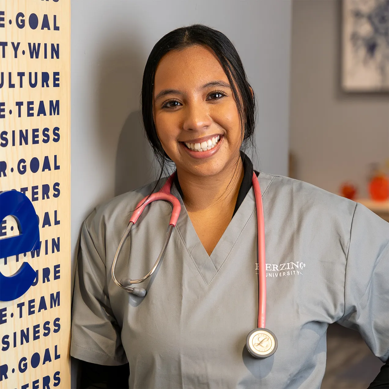 Smiling Herzing University nursing student in scrubs with a stethoscope, standing in a welcoming environment.