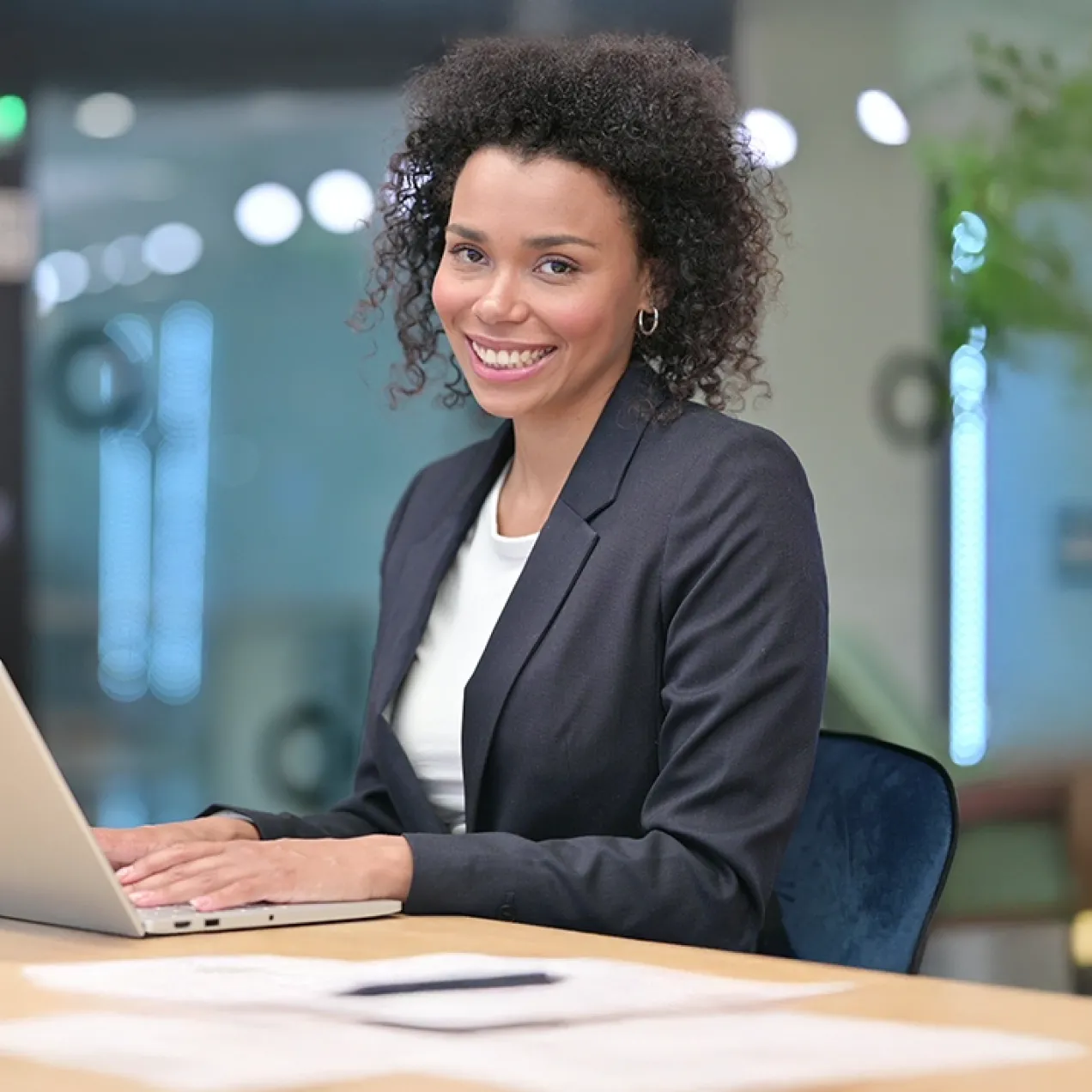 A professional woman sits at a desk with a laptop, smiling confidently, representing career success with a business management degree.