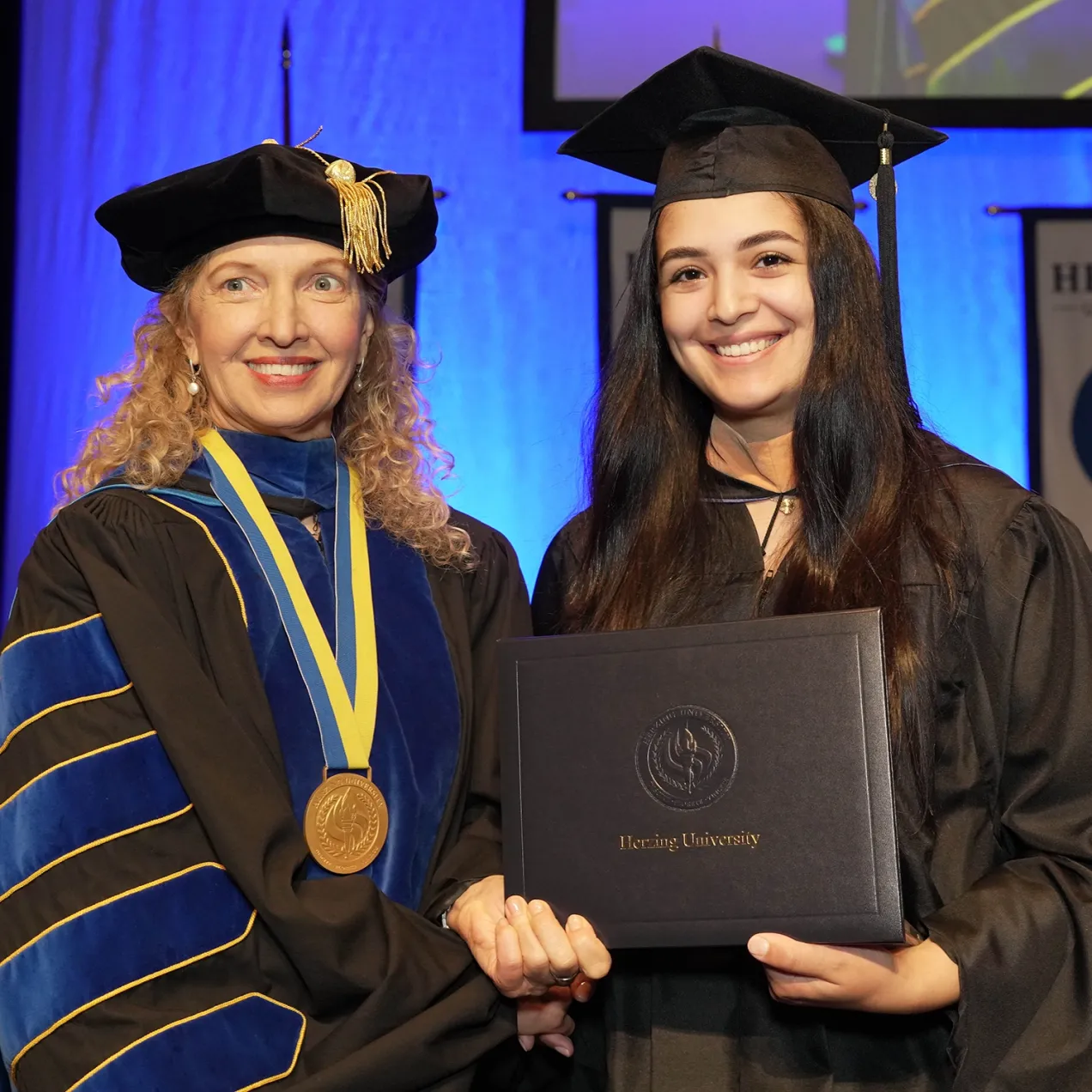Herzing University President Renee Herzing presenting diploma to an international student during graduation ceremony