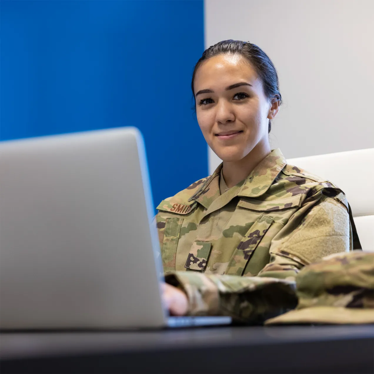U.S. military service member in uniform smiling while using a laptop at a desk