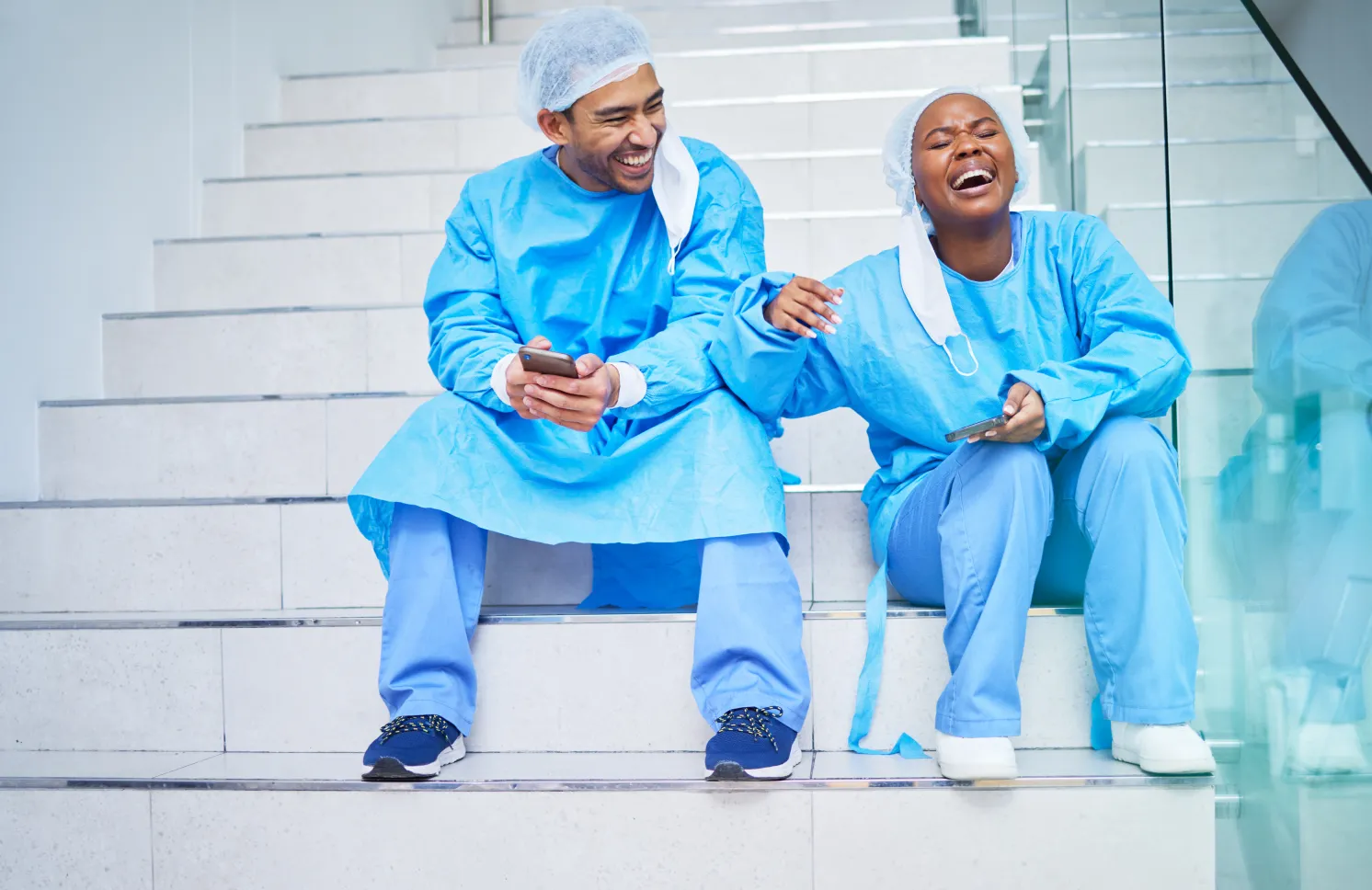 urgeon, conversation and laughing on hospital stairs with phone and funny meme. Healthcare, medical and doctor team relax with comic and conversation together with mobile and social networking