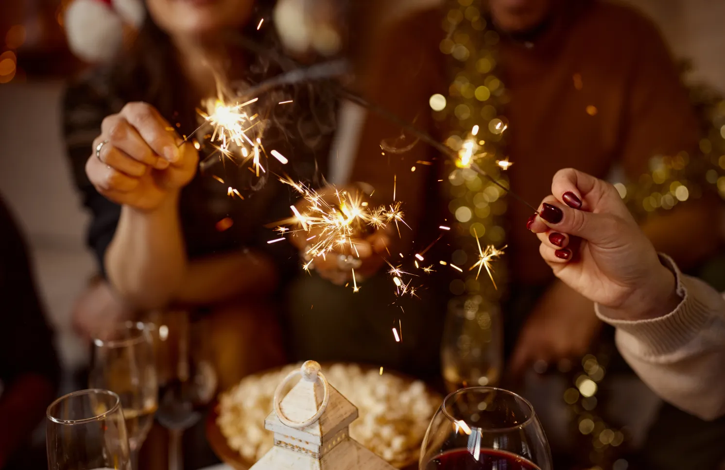 Close up of unrecognizable friends having fun with sparklers while celebrating Christmas at home.