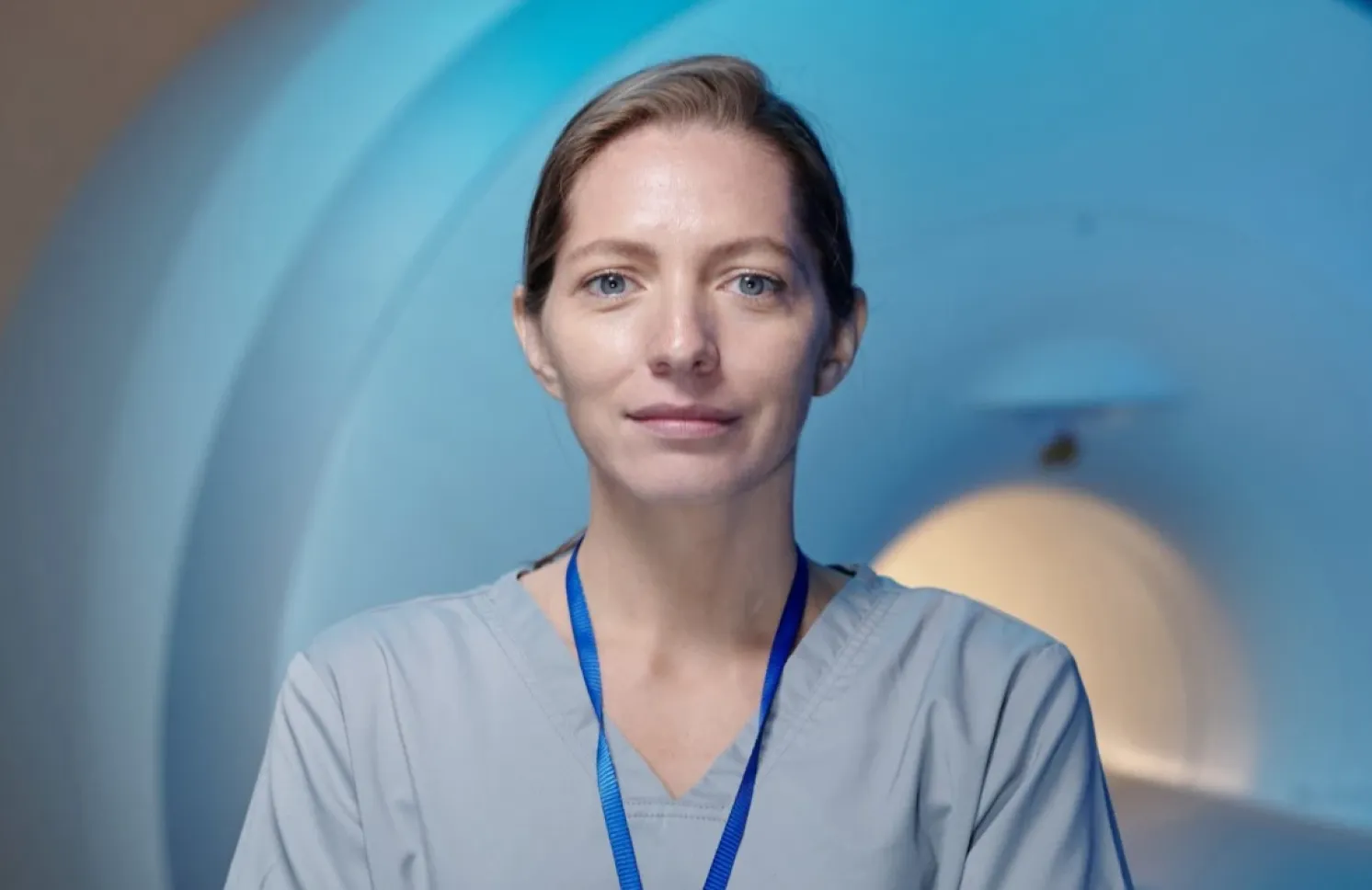Radiologic technologist in scrubs stands in front of a medical imaging machine in a clinical lab.