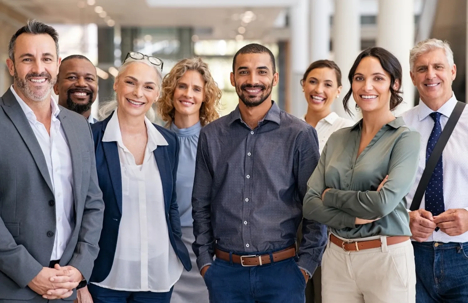 A diverse group of eight smiling business professionals standing together in a bright, modern office.