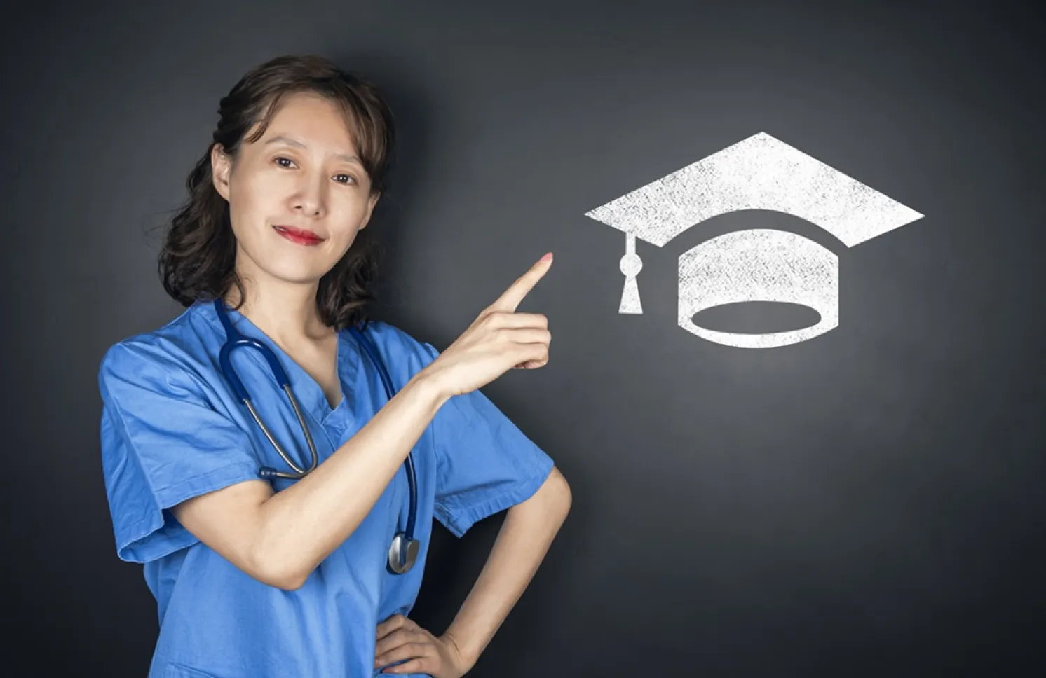 A nurse in blue scrubs points to a graduation cap symbol, representing nursing education, academic achievement, and career advancement.