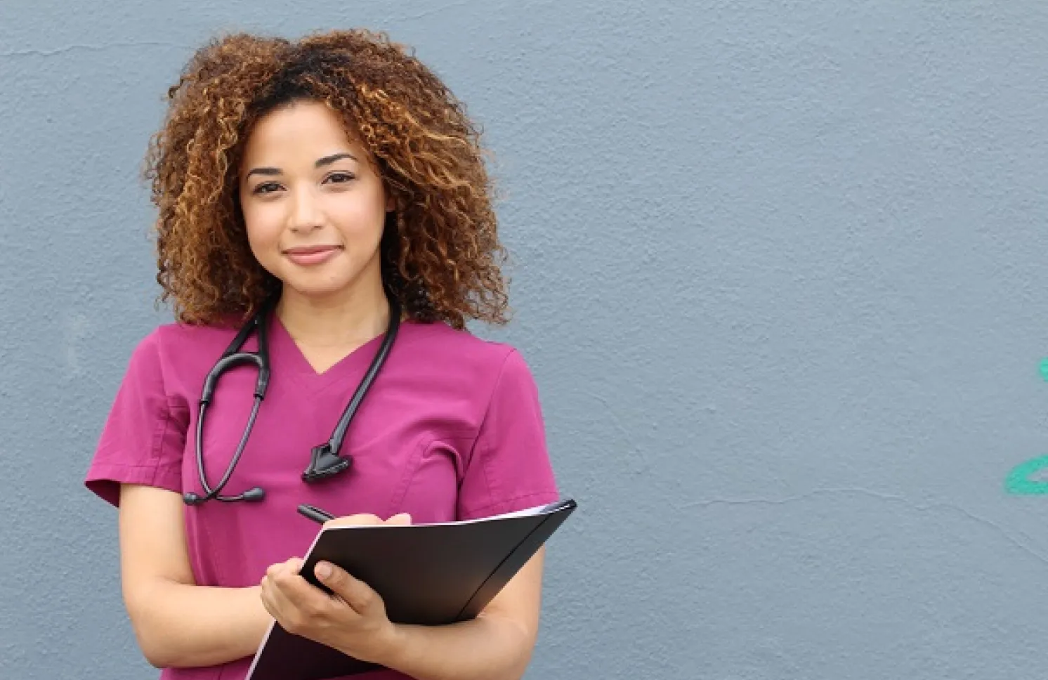 Nurse in pink scrubs who earned a BSN holding clipboard and smiling
