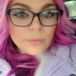 Woman with bright pink hair poses for a selfie in a car
