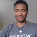 African American man in a Herzing shirt posing for a self in a bedroom