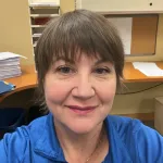 Woman in a blue shirt taking a selfie in an office 