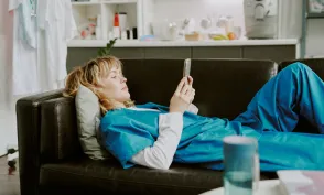 Young Caucasian nurse using smartphone while lying on black leather sofa in on call room