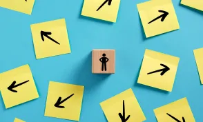 Decision making in business. Choosing a path to follow. Businessman standing on a wooden block, surrounded by arrows pointing in various directions.