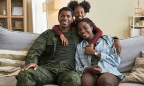 Portrait of African American family of three smiling at camera sitting on sofa with their military dad