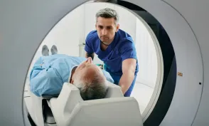 Radiologic technologist positions an older patient on the table of a CT scanner, preparing them for a medical imaging exam.