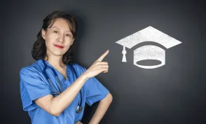 A nurse in blue scrubs points to a graduation cap symbol, representing nursing education, academic achievement, and career advancement.