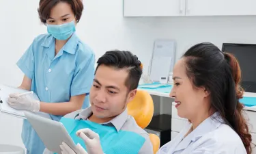 Dental assistant with diploma helping dentist consult with patient