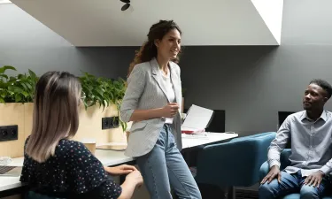 Group of diverse health and human services professionals engaged in a collaborative team meeting in a modern office setting, with one woman standing and speaking while others listen attentively
