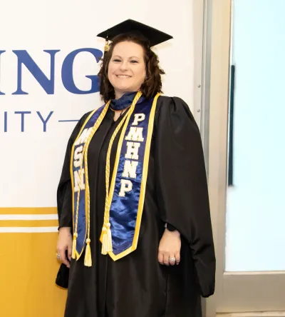 Graduate in cap and gown standing proudly with a PMHNP sash, symbolizing their completion of a Psychiatric Mental Health Nurse Practitioner program.
