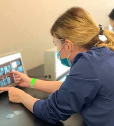 A dental hygiene student examining dental X-rays on a lightbox during hands-on training at Herzing University.