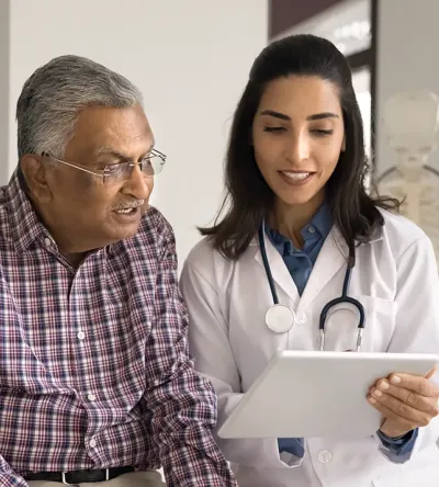 Older patient smiling while a nurse practitioner student reviews health information with him on a tablet
