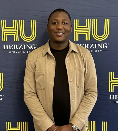 Herzing University international student smiling in front of a branded campus backdrop.