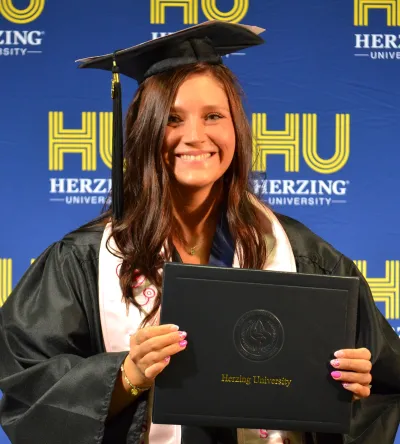 Herzing University graduate proudly holding diploma during commencement celebration