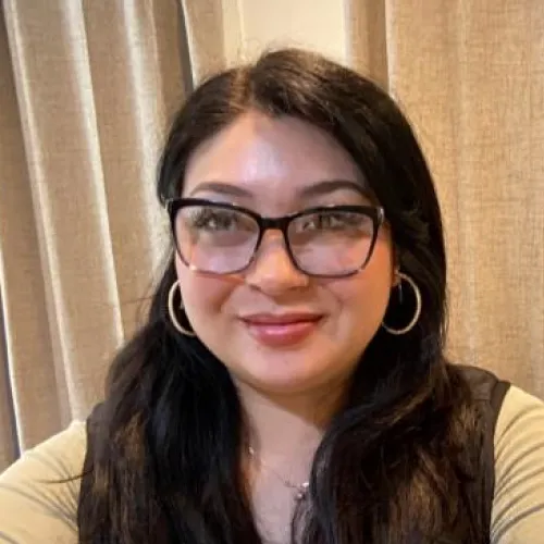 Latina woman in a yellow shirt poses in front of a curtain for a selfie