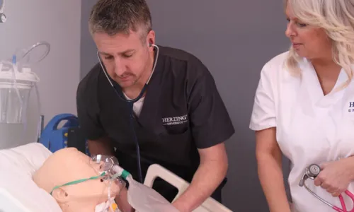 Male nursing student practicing on dummy in simulation labs under supervision of nursing instructor