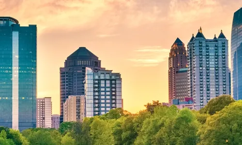 Panoramic view of the Atlanta skyline during sunset with modern skyscrapers and greenery in the foreground.