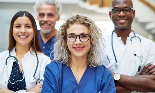 Group of four nurses posing in hospital smiling with arms crossed