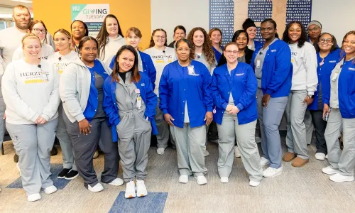 Group of Herzing University Clarksville campus nursing students and faculty wearing scrubs, smiling together inside the campus building.