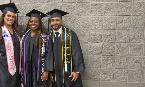 Three Herzing University Tampa campus graduates pose together in caps and gowns at commencement