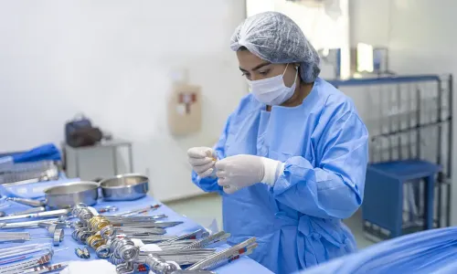 Surgical Technology student in Tennessee wearing protective surgical gown, mask, gloves, and hair covering prepares sterile surgical instruments in a clinical lab setting.