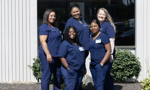ASN students from Herzing University stand together outside a campus building wearing navy blue nursing scrubs.