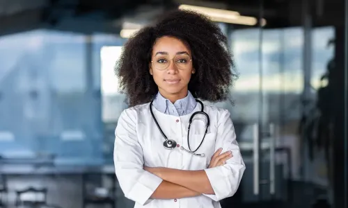 Nurse practitioner student smiling with arms crossed, wearing a white coat Nurse practitioner student smiling with arms crossed, wearing a white coat