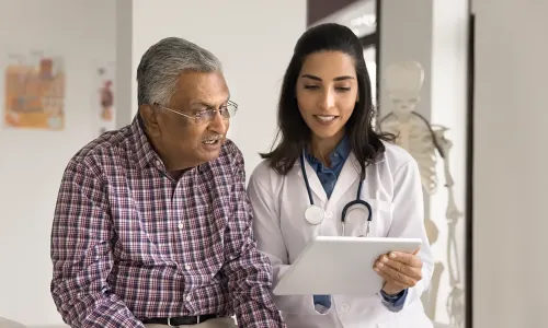Older patient smiling while an adult gerontology acute care nurse practitioner student reviews health information with him on a tablet