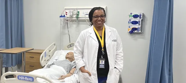 Herzing University nursing instructor in a simulation lab with hospital beds and mannequins.