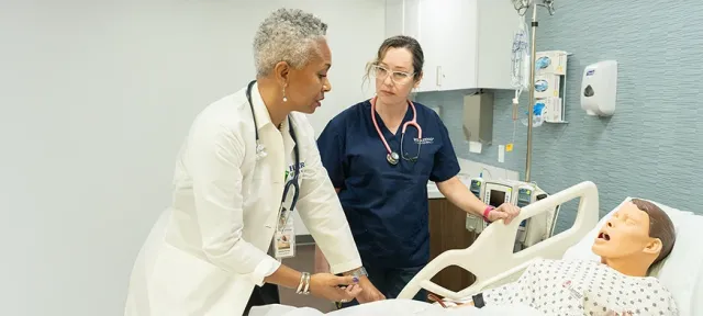 Herzing University nursing instructor guiding a student through a patient care simulation with a medical manikin in a clinical lab setting
