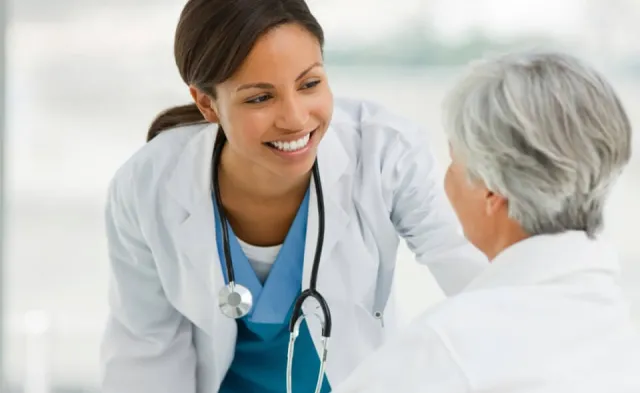 Nurse practitioner smiling while speaking with elderly patient seated in wheelchair