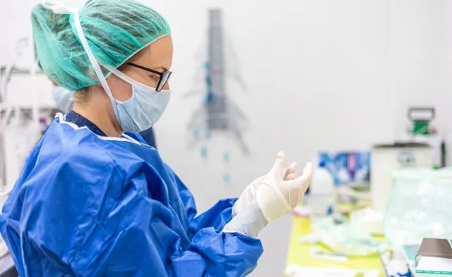 Sterile processing tech wearing mask and additional PPE cleaning surgical instrument in clean room