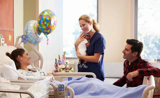 Labor and Delivery Nurse Holding Infant and Smiling with New Parents