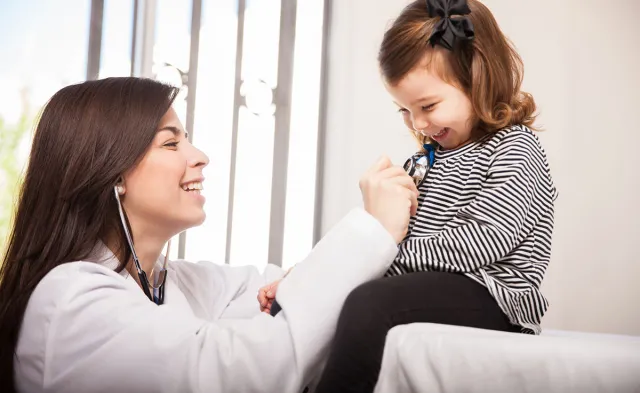 Pediatric Nurse Practitioner Smiling with Young Patient Reading Heart Rate with Stethoscope