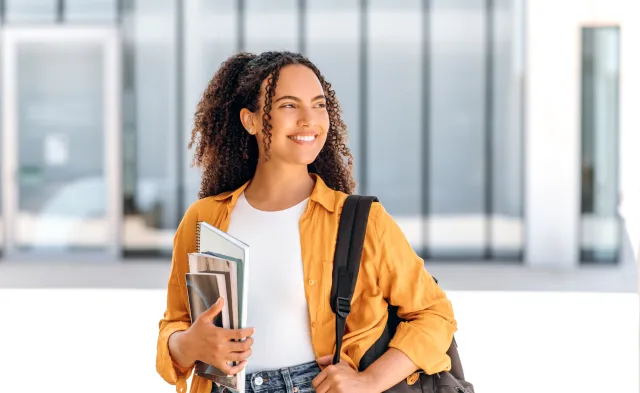 Student wearing backpack and smiling holding textbook