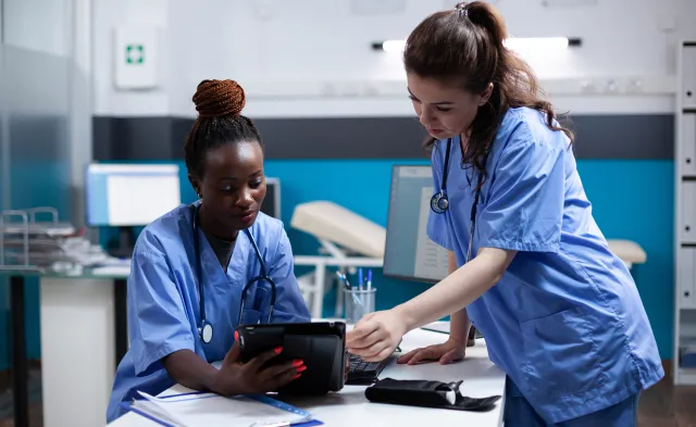 Two medical assistants in blue scrubs viewing patient charts on tablet